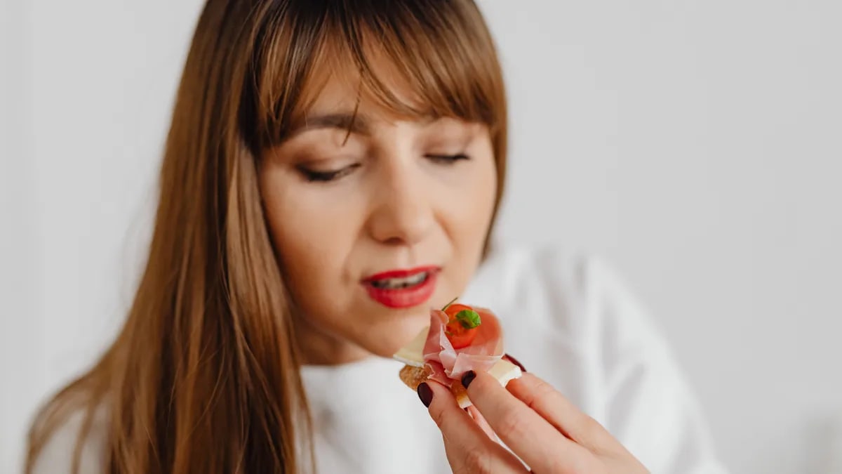 Woman with long hair savoring a gourmet canape indoors.