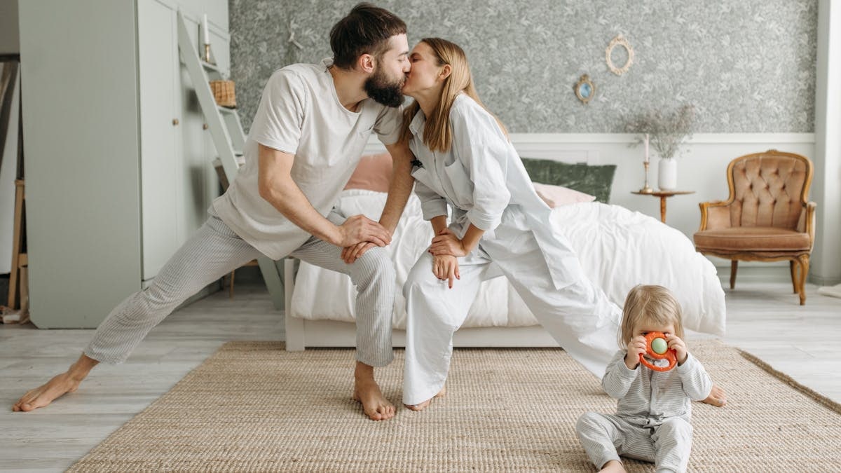 Playful morning with parents stretching and a toddler playing in the bedroom.